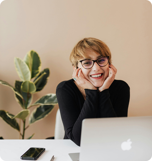 Person smiling behind a laptop in a bright workspace